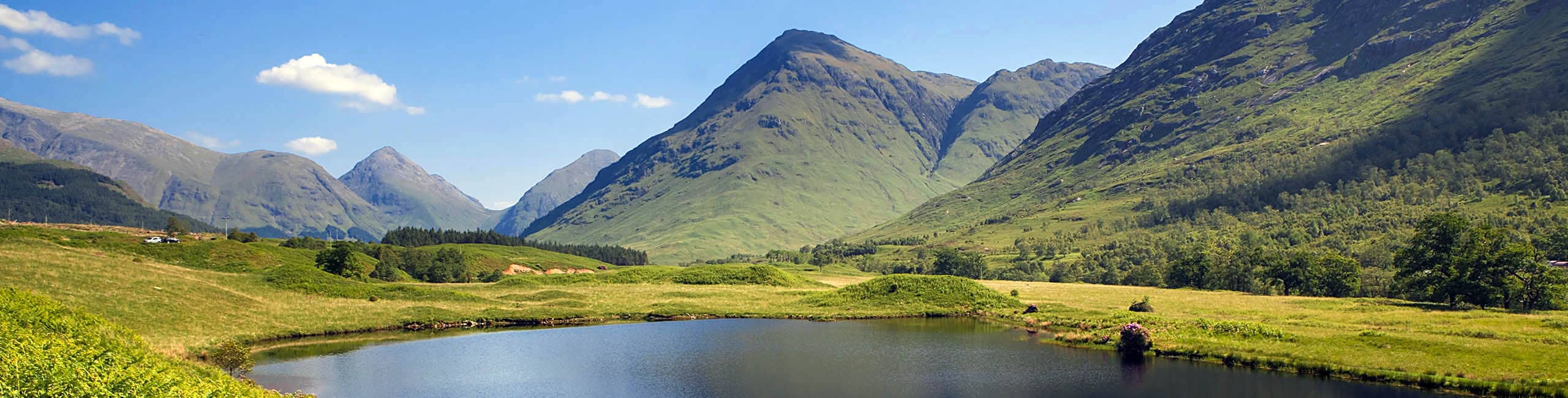 The mountains of Scotland in spring are adorned with lush greenery and feature the tranquil blue waters of the loch.