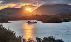 Dramatic sunset view over Loch Awe as the sun sets, casting deep hues of orange and purple across the sky, with silhouettes of trees and hills