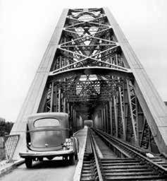 Historical photograph of a railway car on the railway line with an old bridge in the background, featuring a newly added road for cars on the bridge.