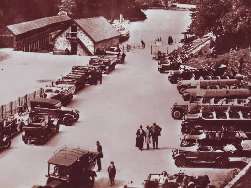 A vintage photograph of the Loch Katrine Pier at the height of the season, showcasing a full car park, reflecting the area's peak popularity