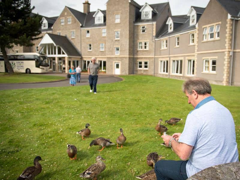 A customer seated on a bench by Loch Tummel, enjoying feeding the ducks