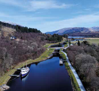 Tranquil view of the Caledonian Canal, with calm waters stretching between lush green banks and distant hills.